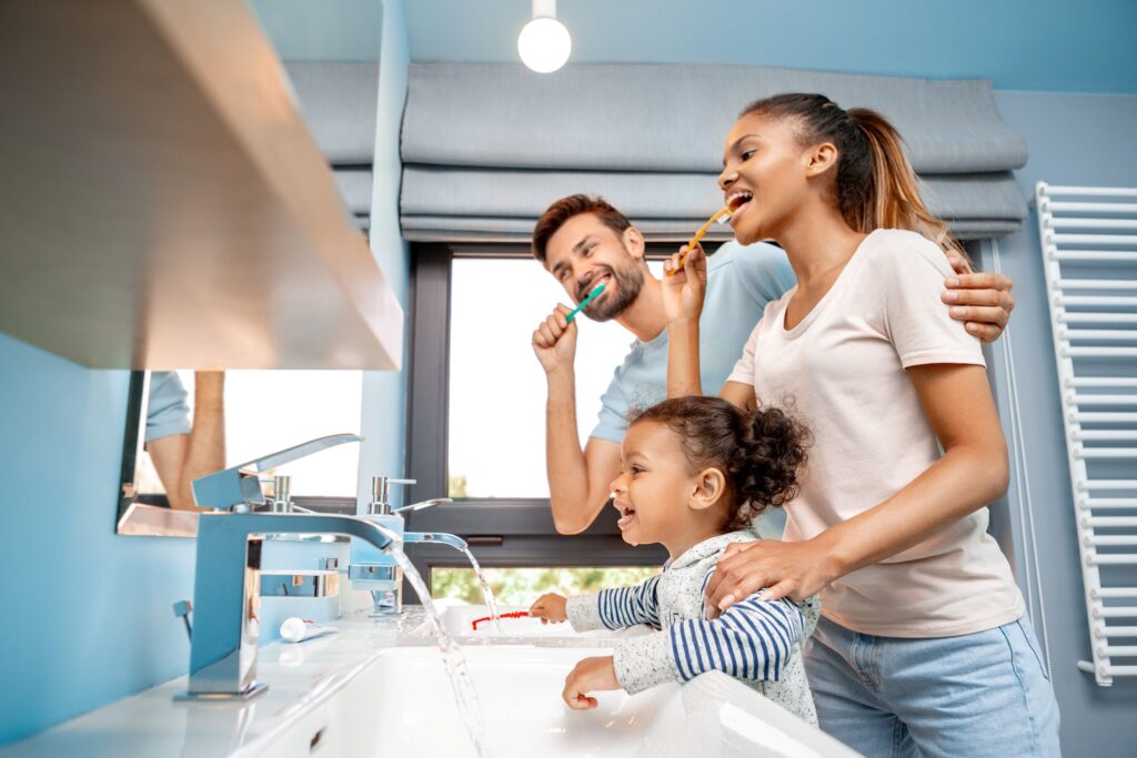Man, woman, and child brushing teeth together at bathroom sink