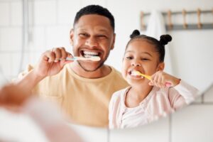 Dad and daughter brushing their teeth together. 